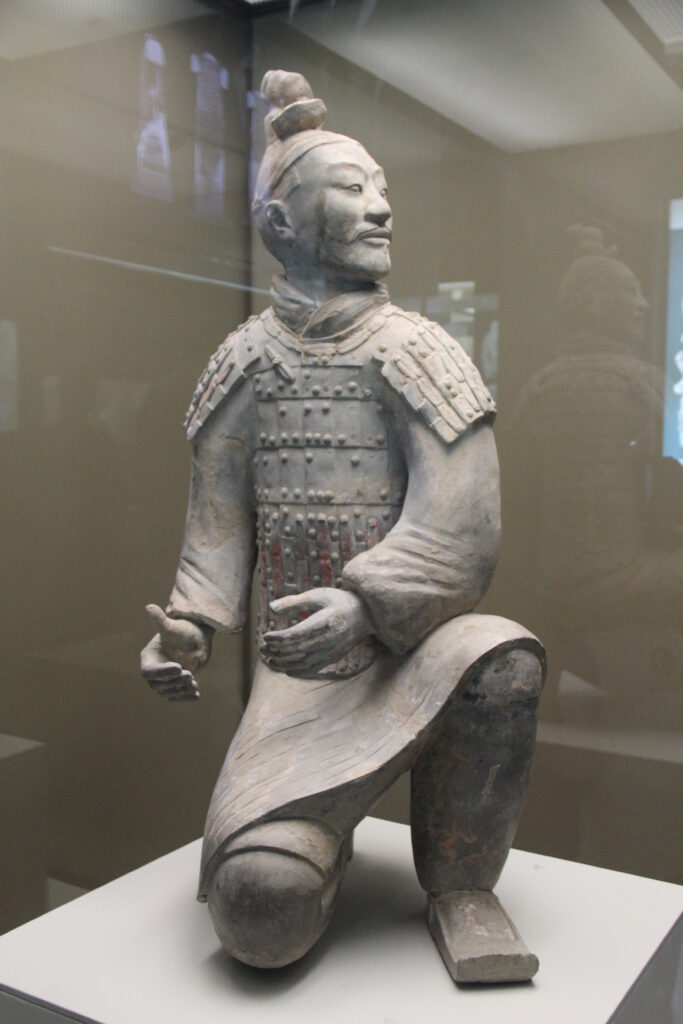 Kneeling terracotta archer with modeled armor and hands held beside the body