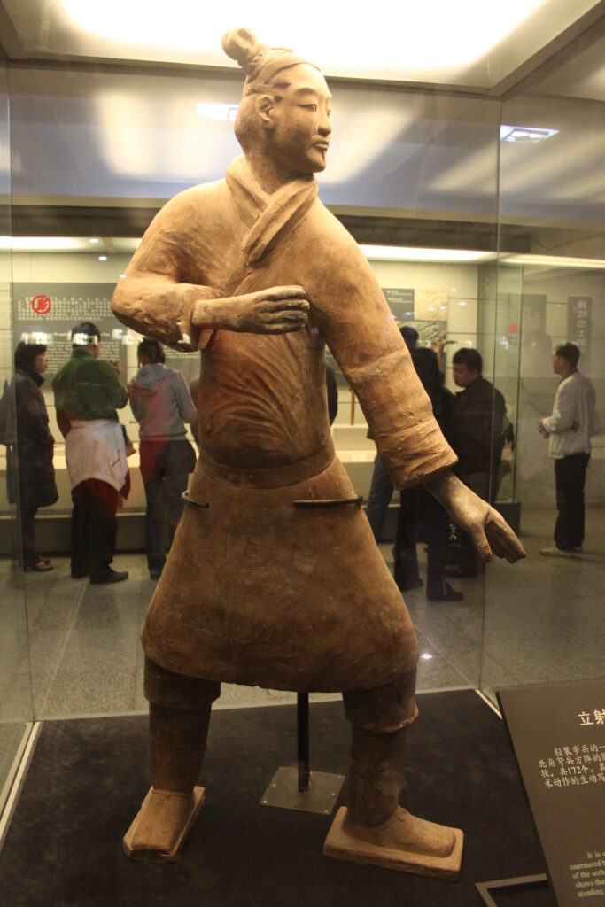 Standing terracotta archer in a belted robe with turned torso and separated feet